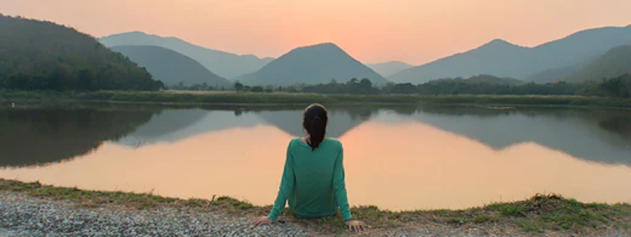 woman sitting at lake staring in distance
