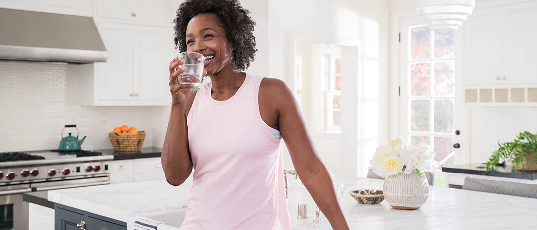 woman drinking out of water glass in kitchen