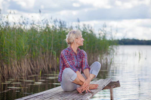 woman sitting next to lake staring into distance